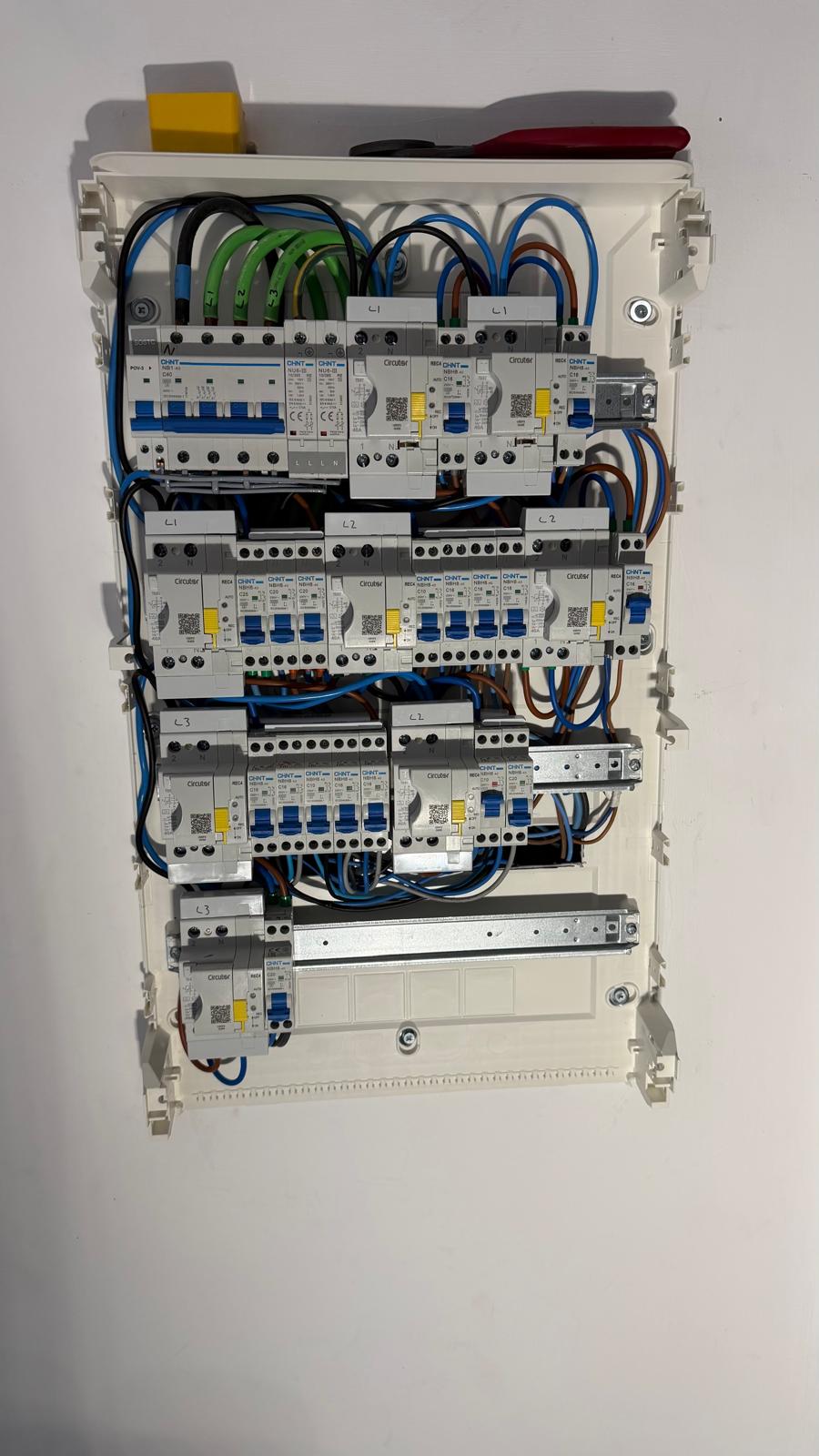 Internal view of the new Chint board pre-assembled off-wall — Chint NB1 four-pole main switch and Chint Type 2 surge protection device on the top row, eight Circutor REC4 self-reclosing 30 mA RCDs (yellow service handles) on the rails below, and the Chint NB1 1P+N Type C MCBs distributed underneath each RCD group. The chassis-side phase labelling — L1, L2, L3 — is visible above each row, showing how the eight RCD groups have been balanced across the three phases of the supply. All flying leads cut to length, ferruled, and torqued with a calibrated torque screwdriver before energising.