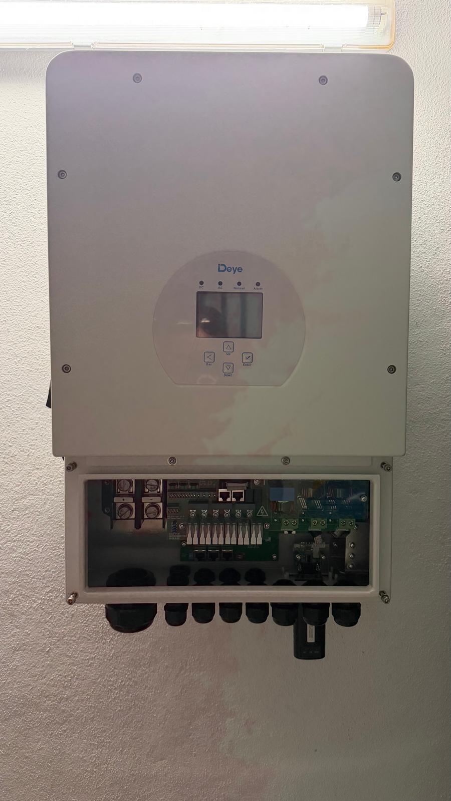Inversor híbrido Deye SUN-10K-SG04LP1 instalado en la pared del cuarto técnico — la bahía de conexiones está abierta mostrando los bornes de CC y CA, puertos de comunicación y prensaestopas. Esta unidad de 10 kW tiene un techo de entrada DC de 12,5 kW, dejando más de 6 kW de holgura para futura ampliación de paneles.