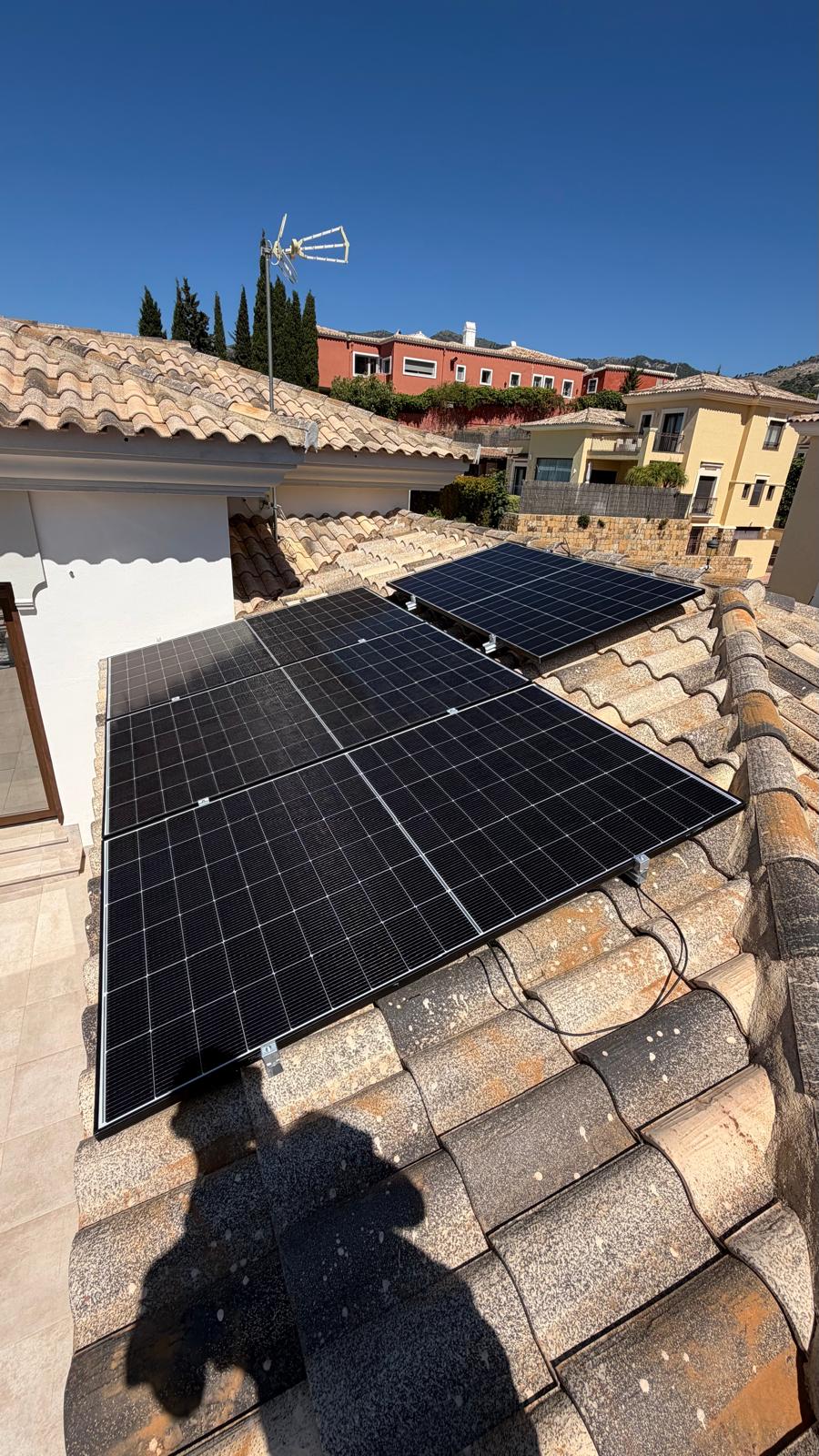 Sección de cubierta superior completada — cuatro paneles mono PERC de 500 W instalados en disposición 2×2 en el plano de la cubierta secundaria, con las villas vecinas y la ladera escalonada detrás. Los cables solares DC están encaminados a lo largo de la hilera de tejas hasta el punto de penetración de cubierta.