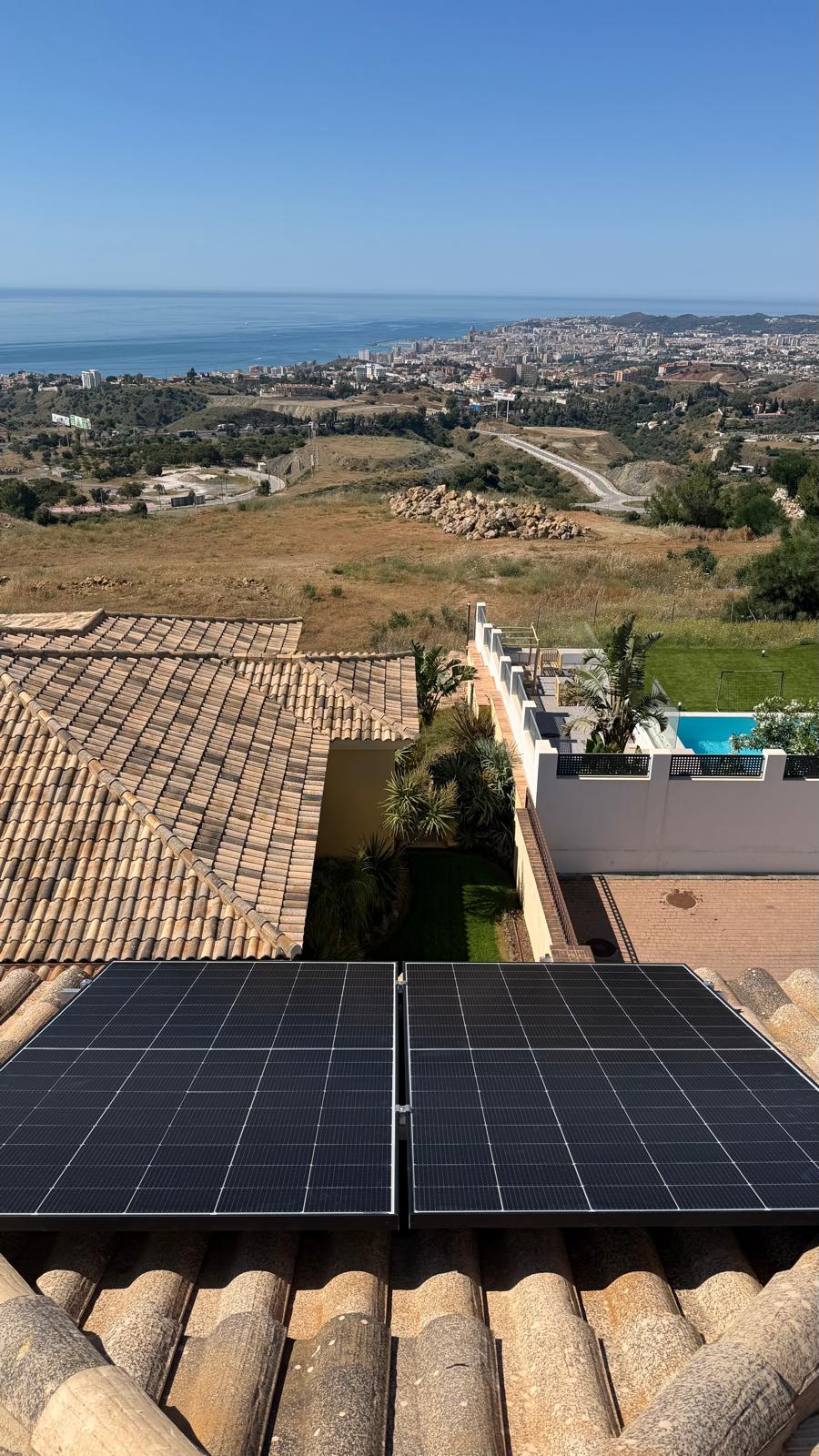 Dos paneles mono PERC de 500 W instalados en la cubierta de tejas de terracota orientada al sur — el mar Mediterráneo y el frente marítimo de Fuengirola son visibles más allá de la piscina y el jardín de la villa. Los paneles se asientan sobre los raíles de montaje de aluminio instalados en la primera fase, sujetos en posiciones central y de extremo.