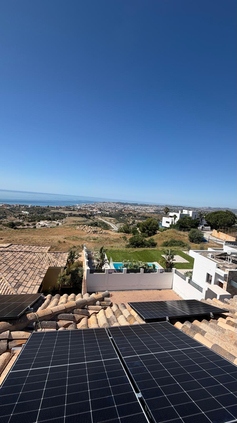 Vista amplia de la instalación de paneles completada — cuatro paneles en la sección principal de cubierta orientada al sur con la piscina de la villa claramente visible en el centro-izquierda y la Costa del Sol extendiéndose hasta el horizonte. La segunda sección de cubierta (borde derecho) alberga los paneles restantes de la instalación de 12 paneles.