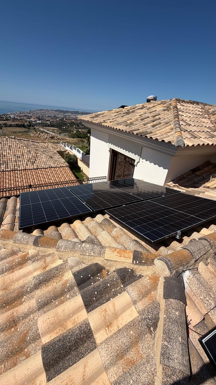 Cuatro paneles instalados en la sección de cubierta inferior adyacente a la terraza superior de la villa — esta sección utiliza la segunda entrada MPPT del inversor Deye, pre-puesta en marcha y lista para aceptar paneles adicionales cuando el cliente amplíe la instalación. La puerta de la terraza y el enlucido blanco del exterior de la villa son visibles a la izquierda.