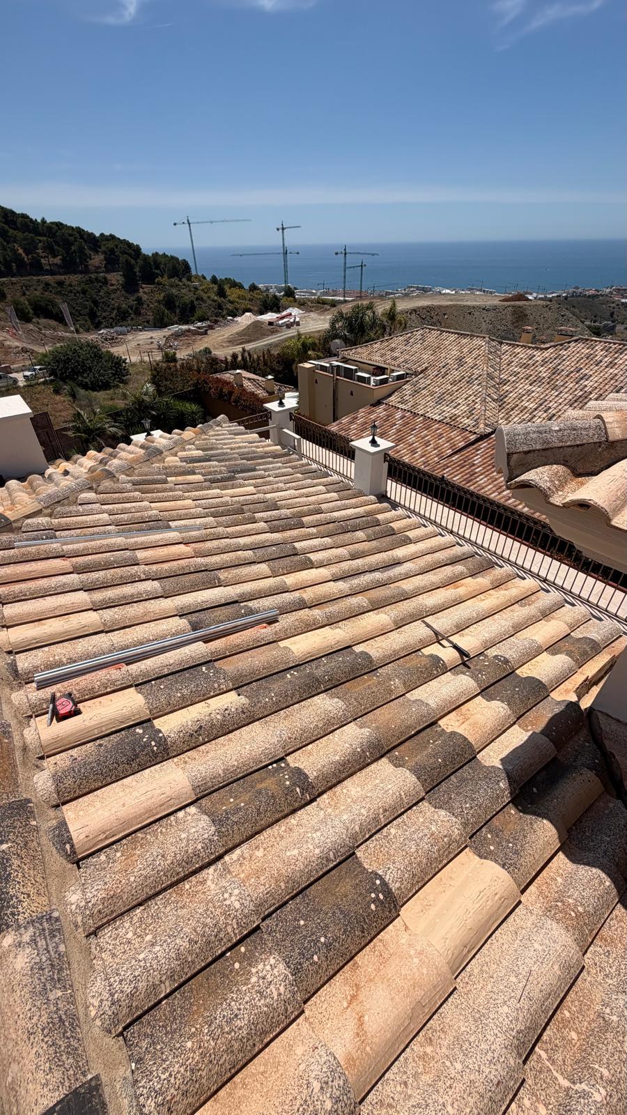 Vista amplia de la cubierta mostrando la distribución de raíles de montaje en el plano sur — grúas de construcción en la costa de Mijas visibles al fondo. El plano de cubierta nivelado y sin obstáculos confirmado durante el levantamiento como apto tanto para la instalación inicial de 6 kWp como para la futura ampliación prevista en la sección adyacente.