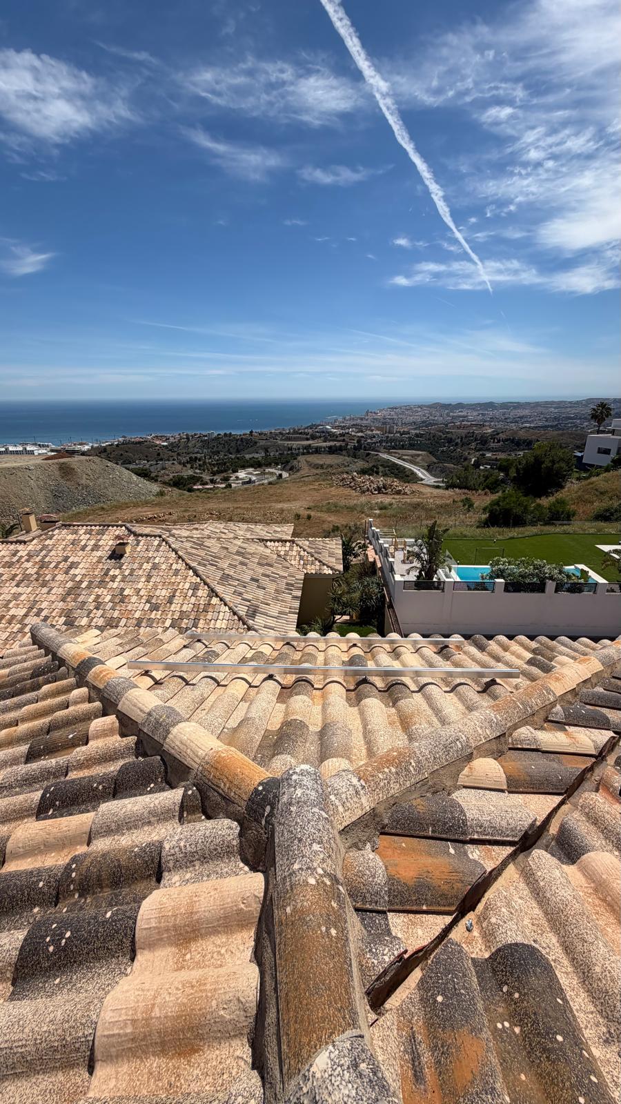 Vista desde la cumbrera mostrando la unión entre los dos planos de cubierta — el plano principal orientado al sur (primer plano) y la sección adyacente identificada para la futura ampliación de paneles. La costa de Mijas, Fuengirola y el Mediterráneo son visibles a lo lejos, confirmando la exposición sur sin obstáculos en toda la instalación.