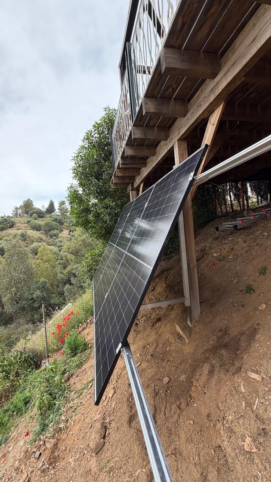Vista lateral del primer panel montado — el plano del panel queda con una inclinación aproximada de 25°, algo más tendida que el ángulo óptimo por latitud para Mijas, elegido deliberadamente porque la orientación suroeste se complementa mejor con una inclinación más tendida para ensanchar la curva de producción de la tarde, en lugar de maximizar el pico al mediodía solar. Los tirantes diagonales que se pierden en la ladera a la derecha del encuadre anclan la estructura frente a la succión por viento en rachas de Levante.