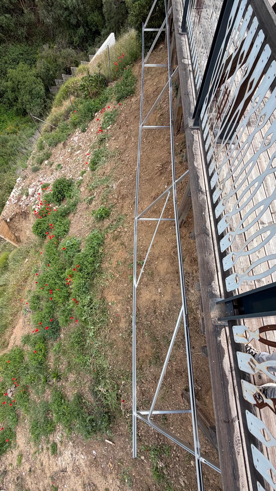 Vista en planta desde la terraza superior mostrando la estructura de acero a lo largo del borde inferior de la terraza — el plano de la futura instalación de paneles sigue la orientación suroeste para una curva de producción extendida por la tarde. El terreno que cae a la izquierda del encuadre es la pendiente típica de Mijas que hace inadecuados los sistemas estándar de montaje en suelo aquí.