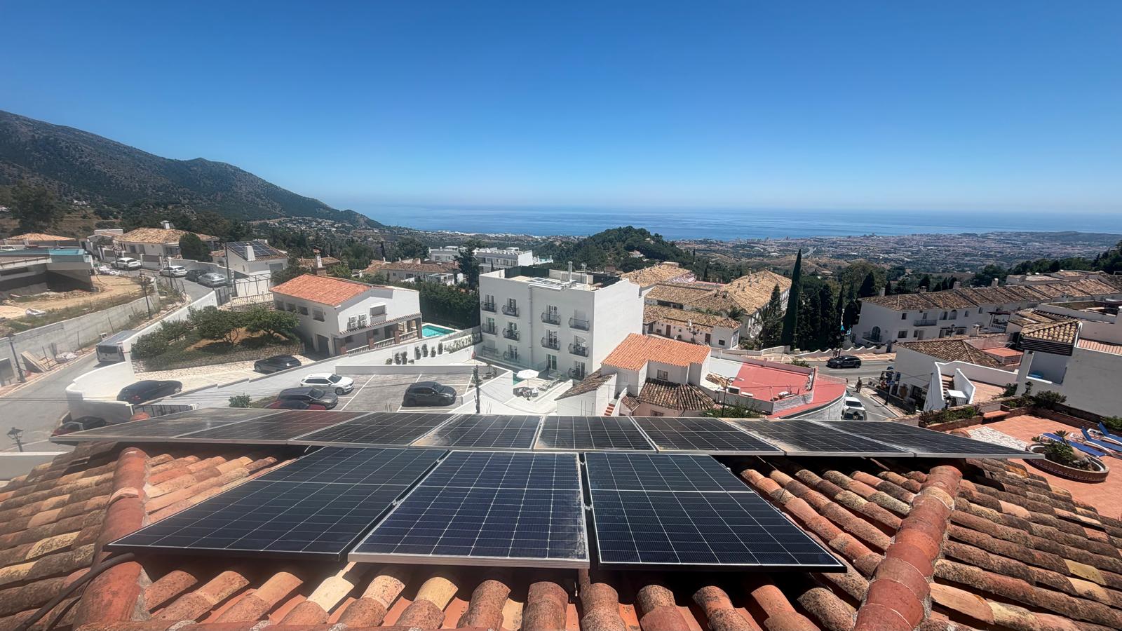 Instalación casi completa vista desde los tejados de Mijas Pueblo — la Sierra de Mijas visible a la izquierda, la costa mediterránea a la derecha. Tejados de teja roja tradicional del pueblo abajo.