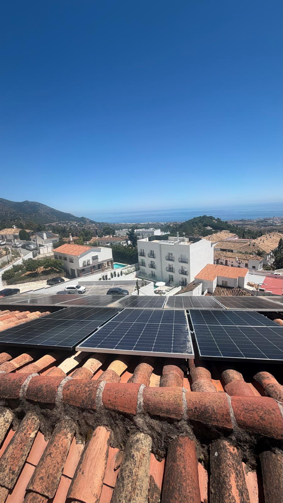 Cuatro paneles correctamente montados y asegurados sobre raíles de aluminio — la costa de la provincia de Málaga visible a lo lejos. Tejas árabes de la propiedad de Mijas Pueblo en primer plano.
