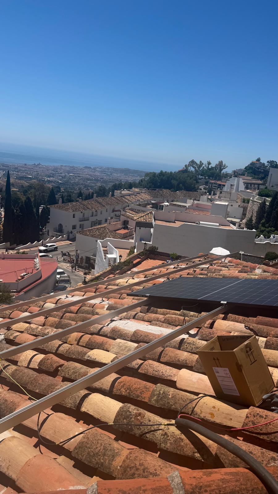 Fase inicial de la reinstalación — raíles de montaje de aluminio colocados sobre el tejado de teja árabe tradicional. La costa mediterránea se extiende en el horizonte detrás de los tejados del pueblo de Mijas.
