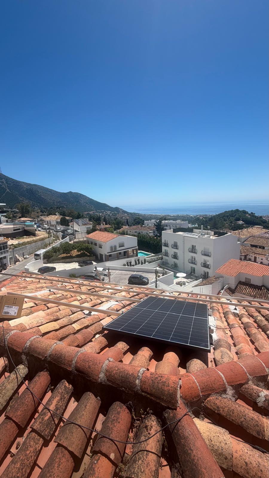 Reinstalación en curso — un panel asegurado sobre los nuevos raíles de aluminio con la terraza de la piscina de la propiedad abajo y el Mar Mediterráneo extendiéndose hasta el horizonte más allá de los tejados encalados de Mijas Pueblo.